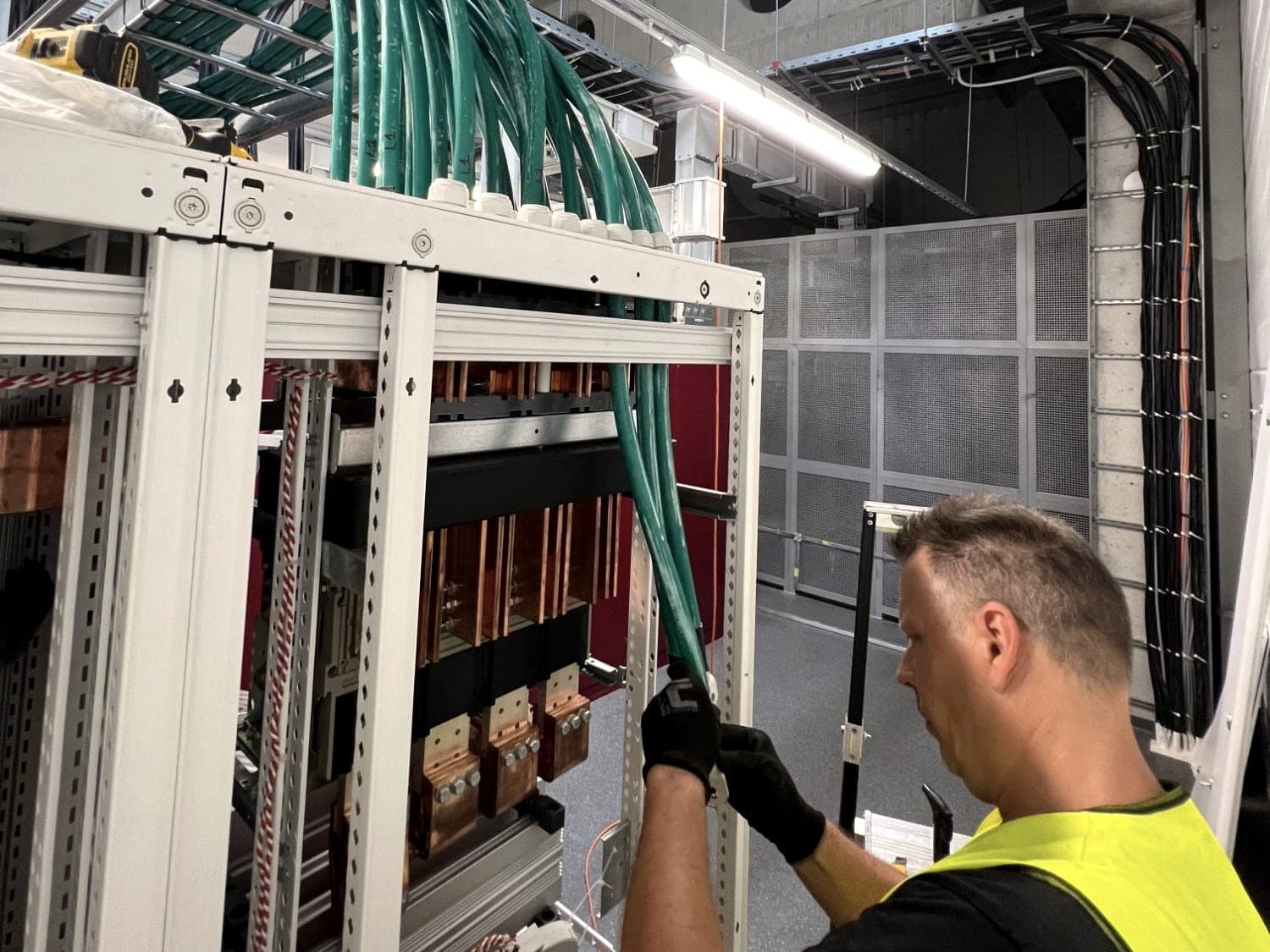 Elektrikár zapája silové káble do hlavného rozvádzača NN s medenými prípojnicami