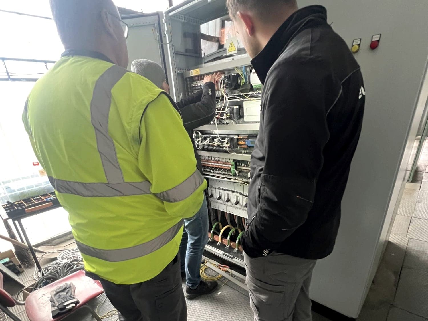 Traja technici pri otvorenom riadiacom rozvádzači počas servisného zásahu